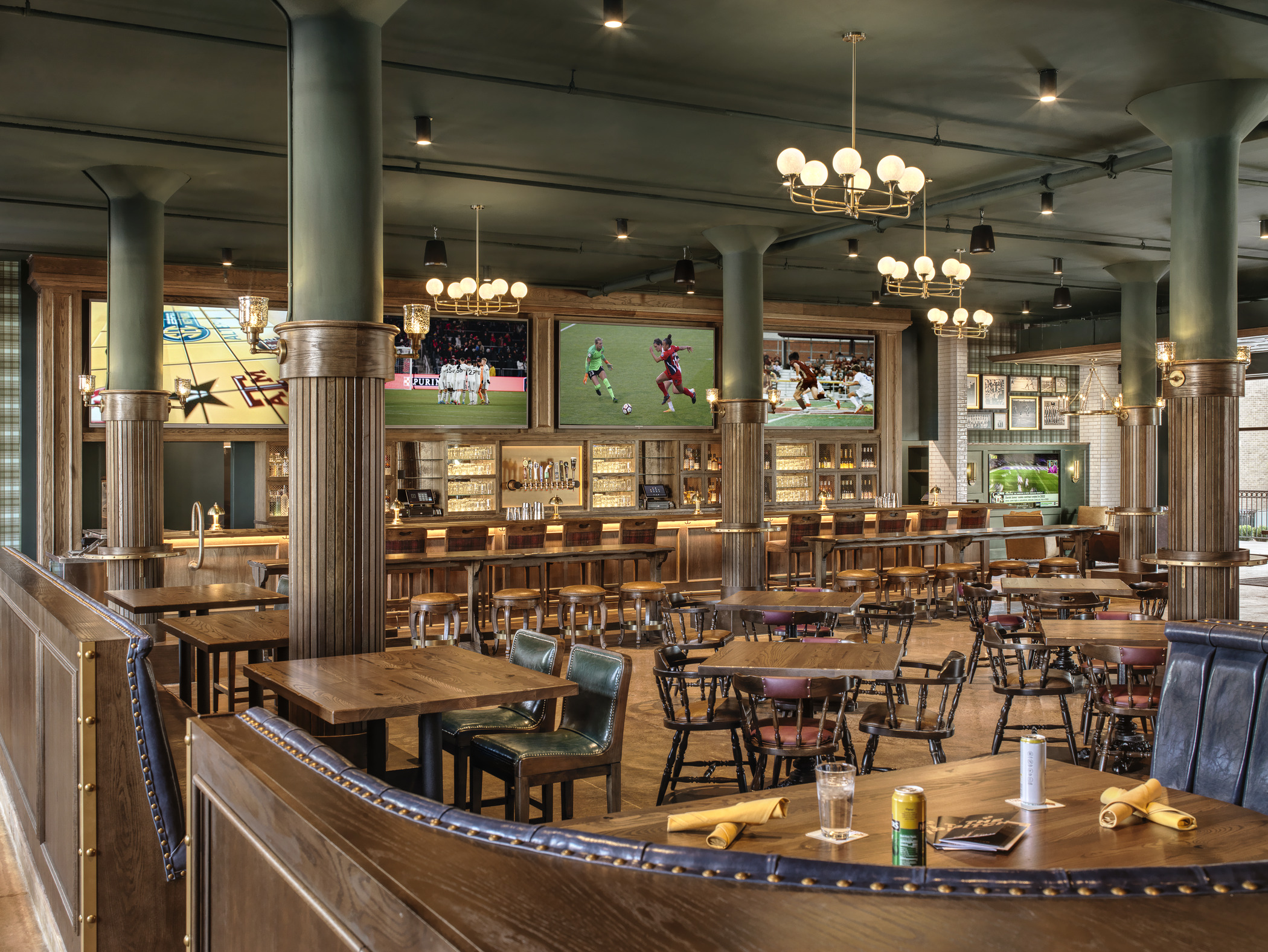 Lush wooden furniture fills an inviting lounge space, with soccer matches playing on TVs over the bar in the rear of the space