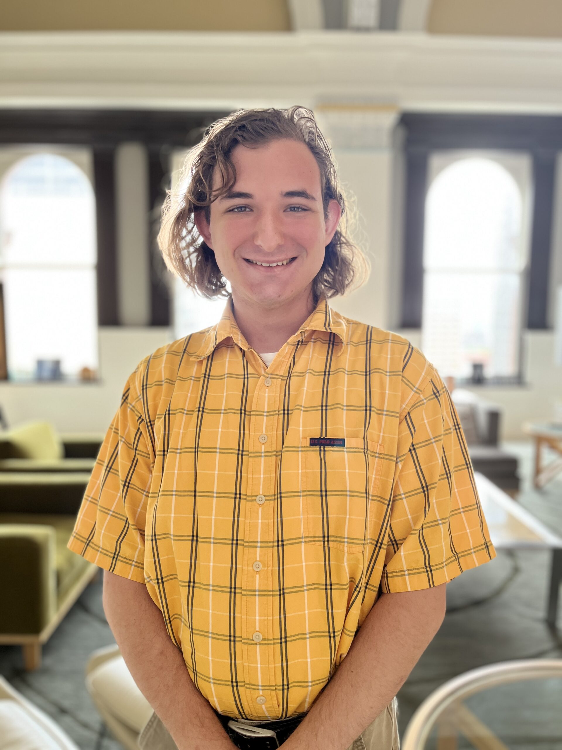 A young man wearing a yellow shirt smiles in a spacious, bright room