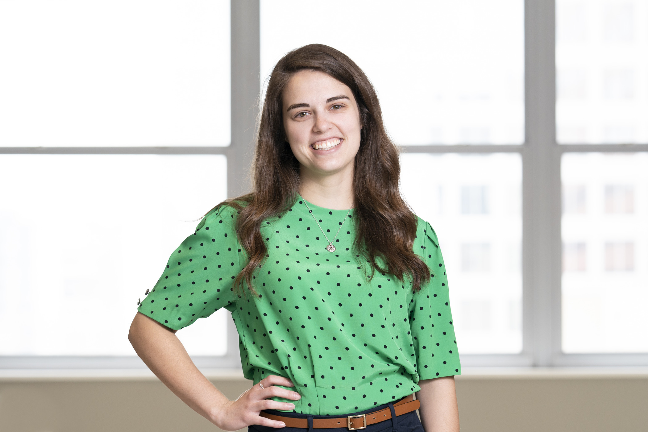 A young woman wearing a green shirt smiles in front of a series of bright windows