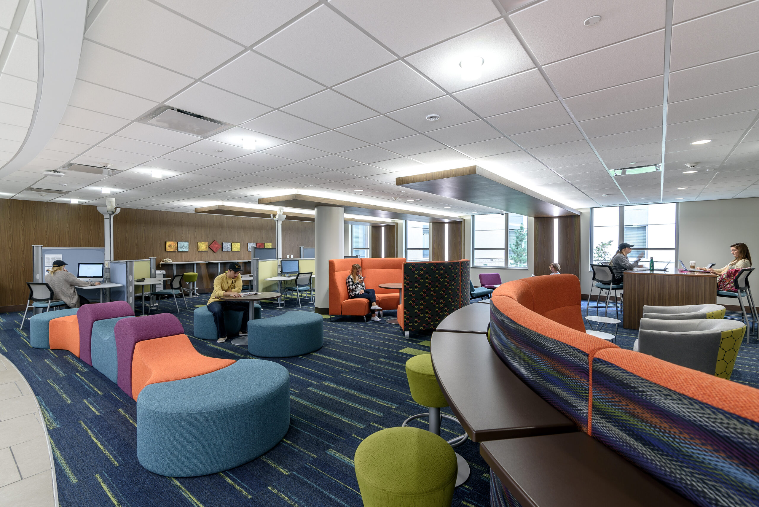 A number of college students relax, study, and work in a spacious, well-lit lounge area