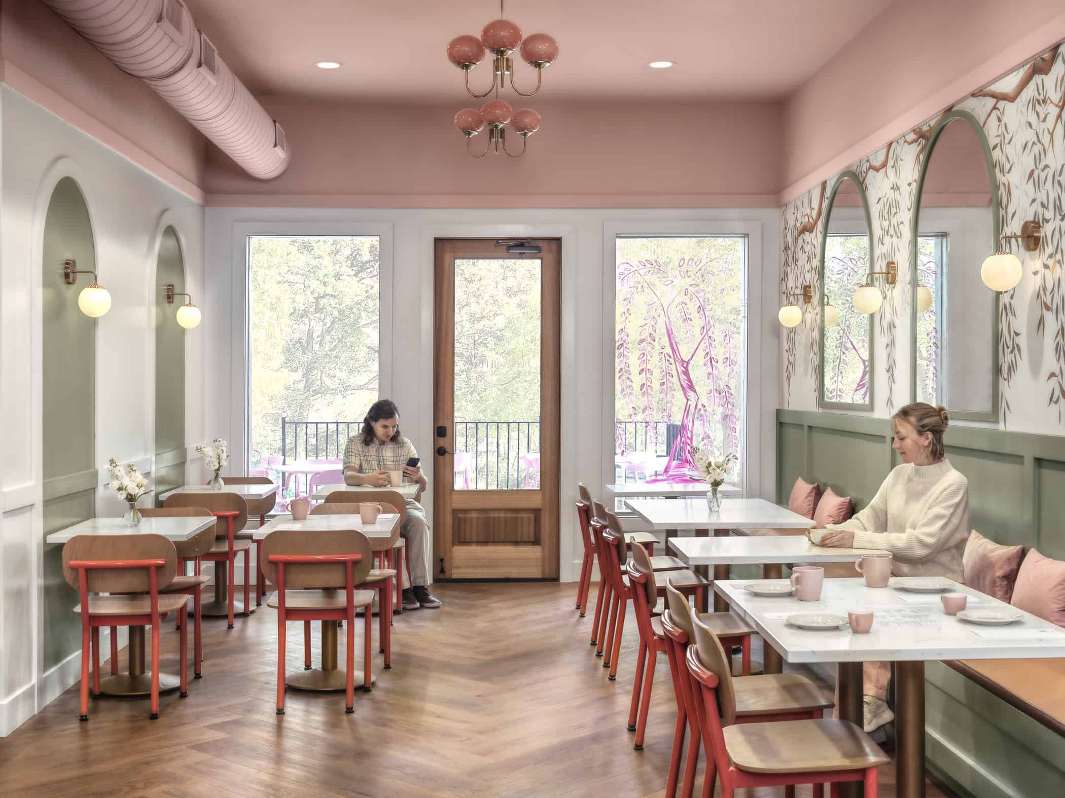 Two diners sit in a pink cafe setting on a sunny day