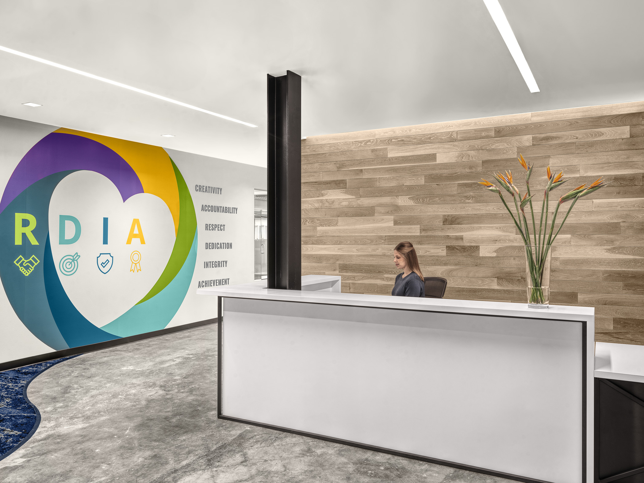 A women sitting at the reception desk across a wall highlighting company values at Lochmueller Group's company values painted on the wall.