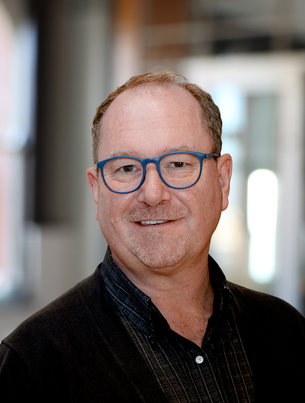 A man with glasses smiles for a professional headshot
