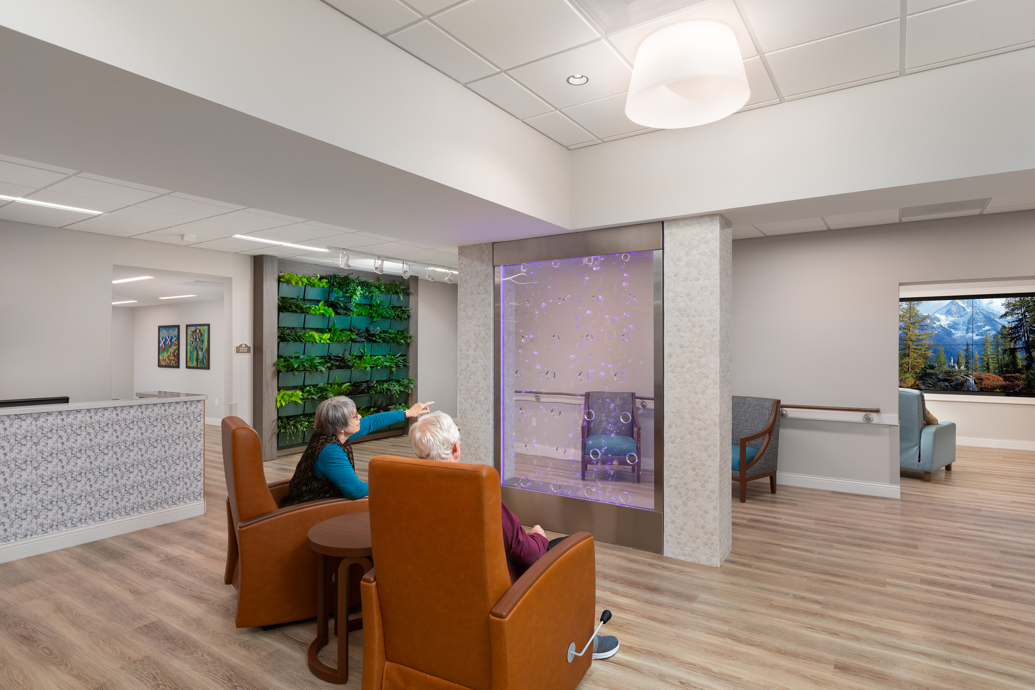 Two seniors sit in lounge chairs while watching a bubble wall.