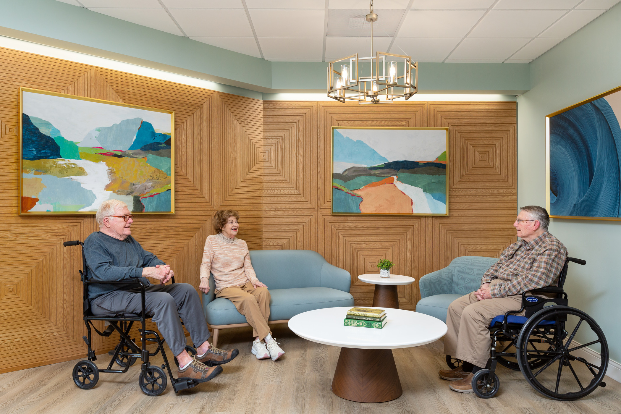 A group of seniors relax around a wood paneled lounge with pastel artwork