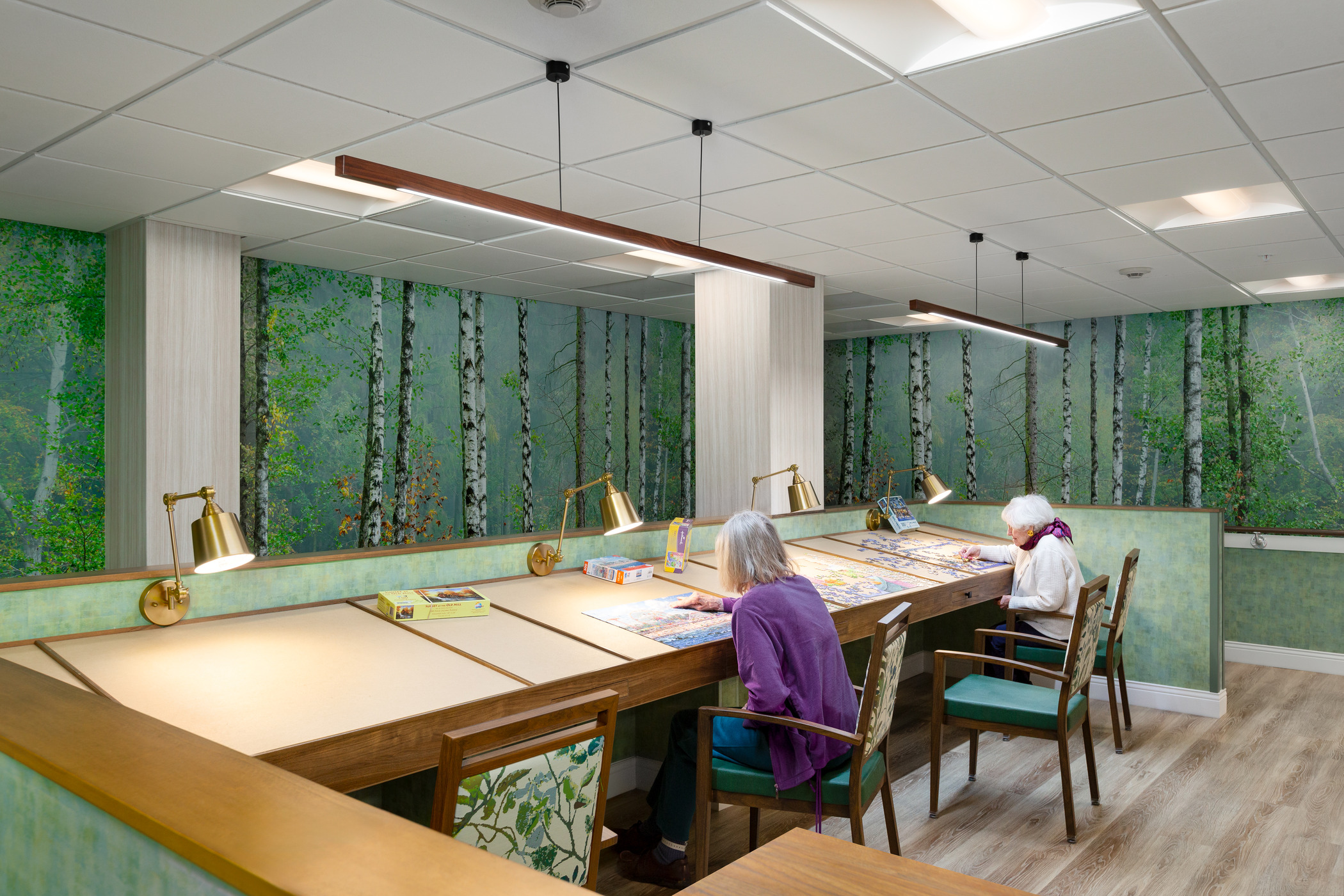 Two senior women assemble puzzles in a room themed to look like a lush forest