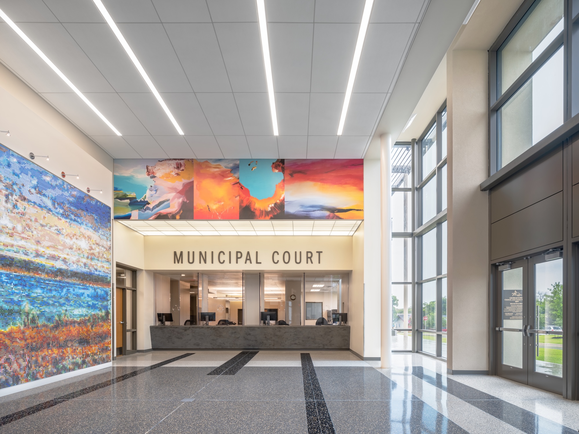 A photograph of an interior space. The back of the photo has a awning that says municipal court and has a colorful mural over the sign