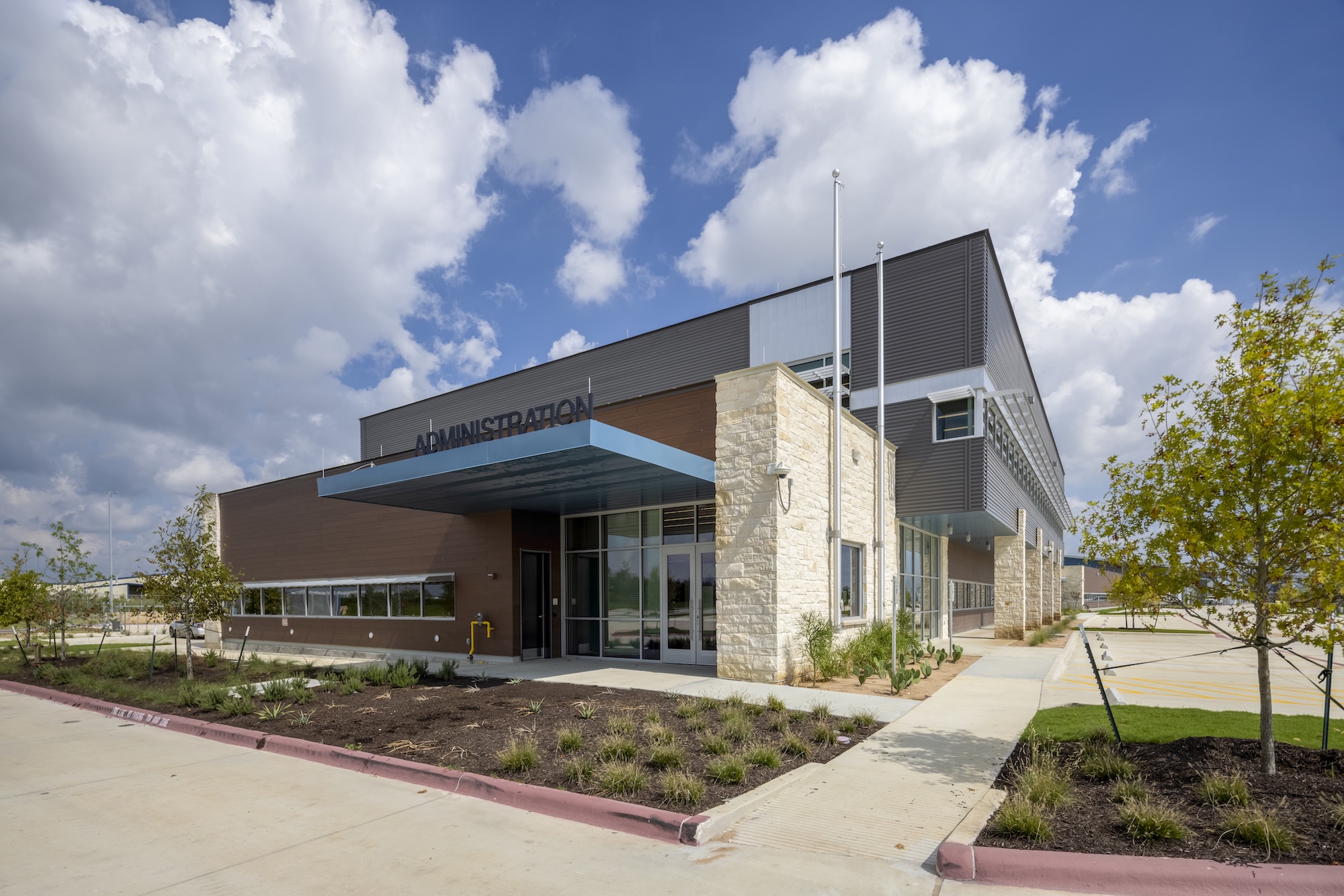 A photograph of a modern building shot from a distance facing the corner. The sky is blue with clouds in it