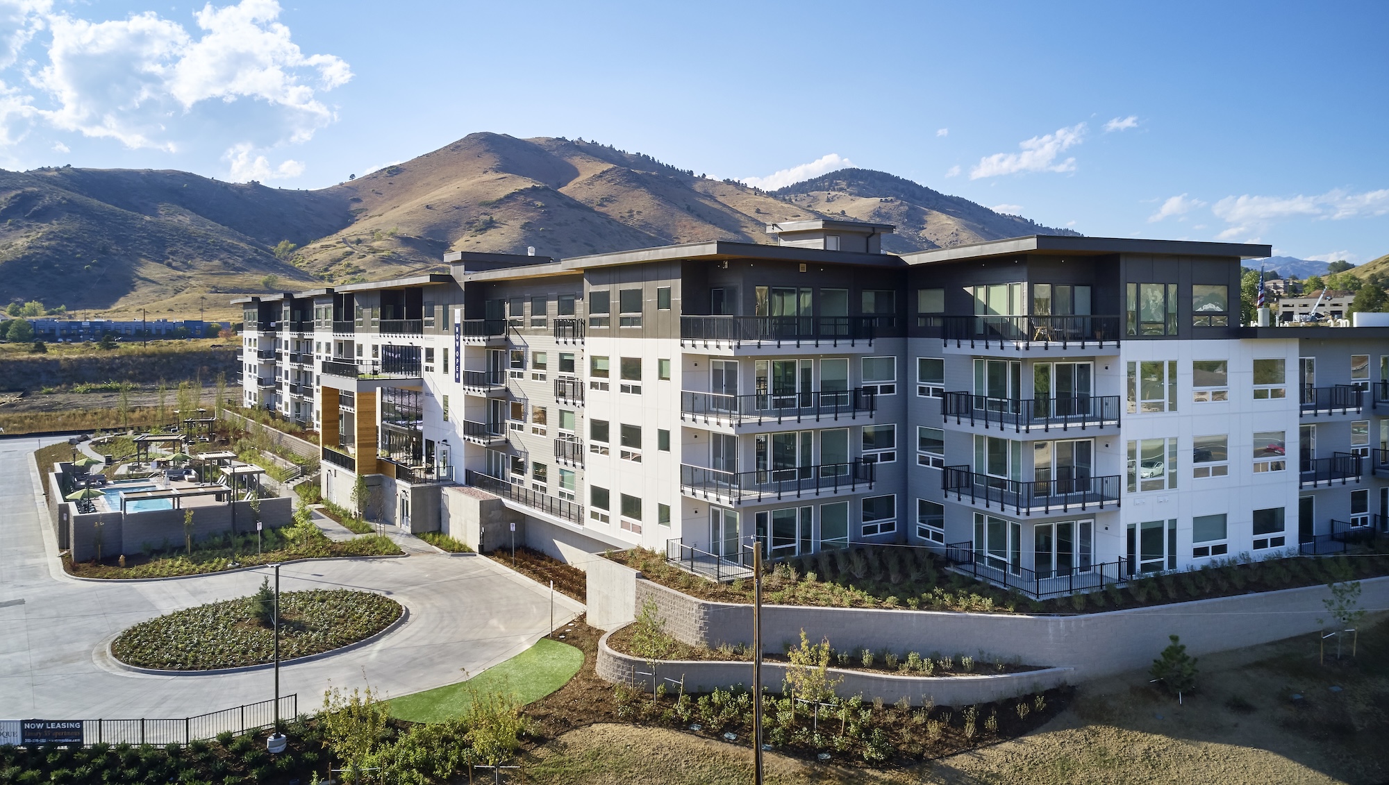 a photograph of the exterior of a large building with a swimming pool. The building is in front of a mountain.