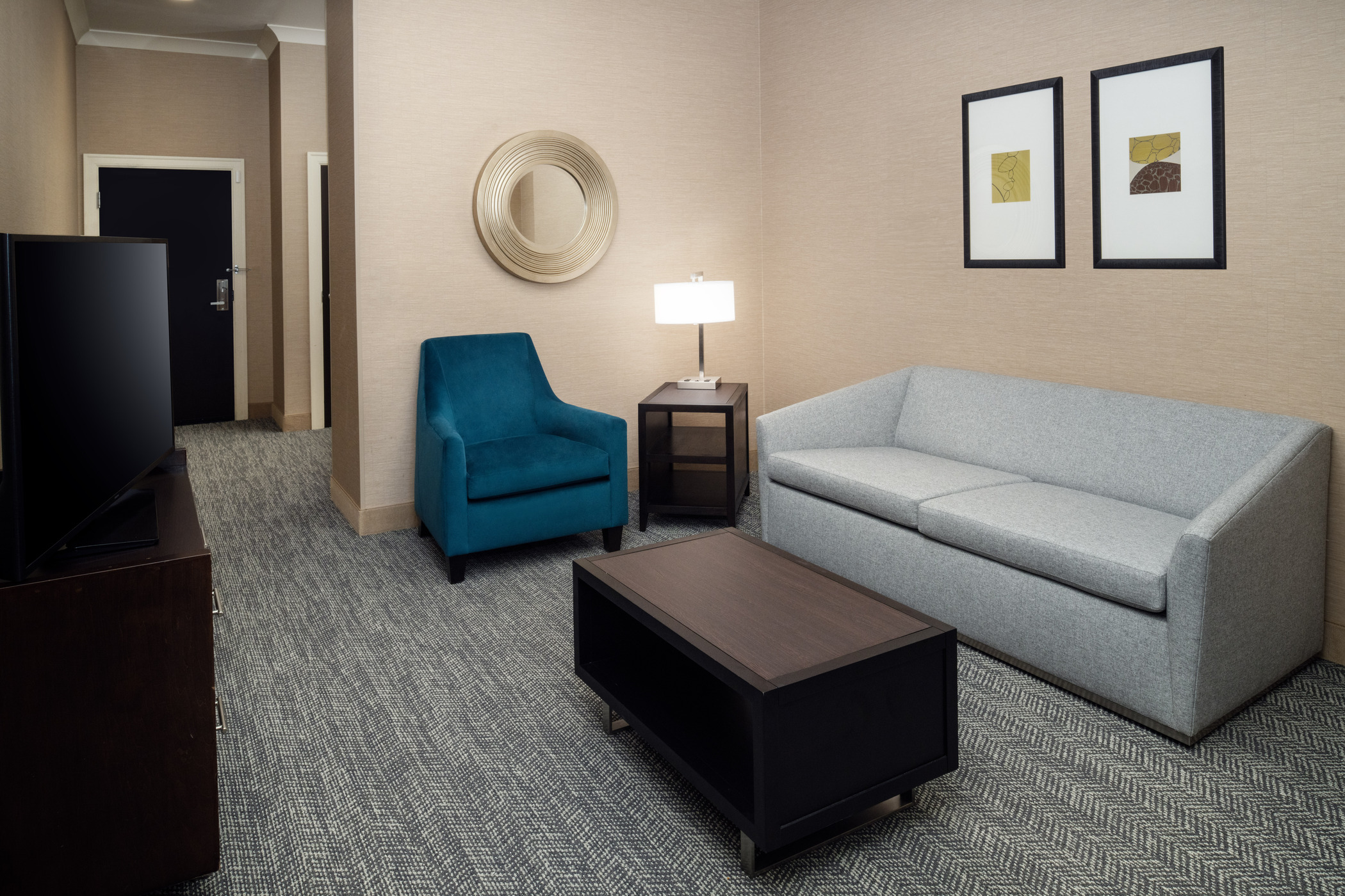 A brown coffee table with gray couch on the right side and a teal armchair to the left, with an end table and a lamp in between.