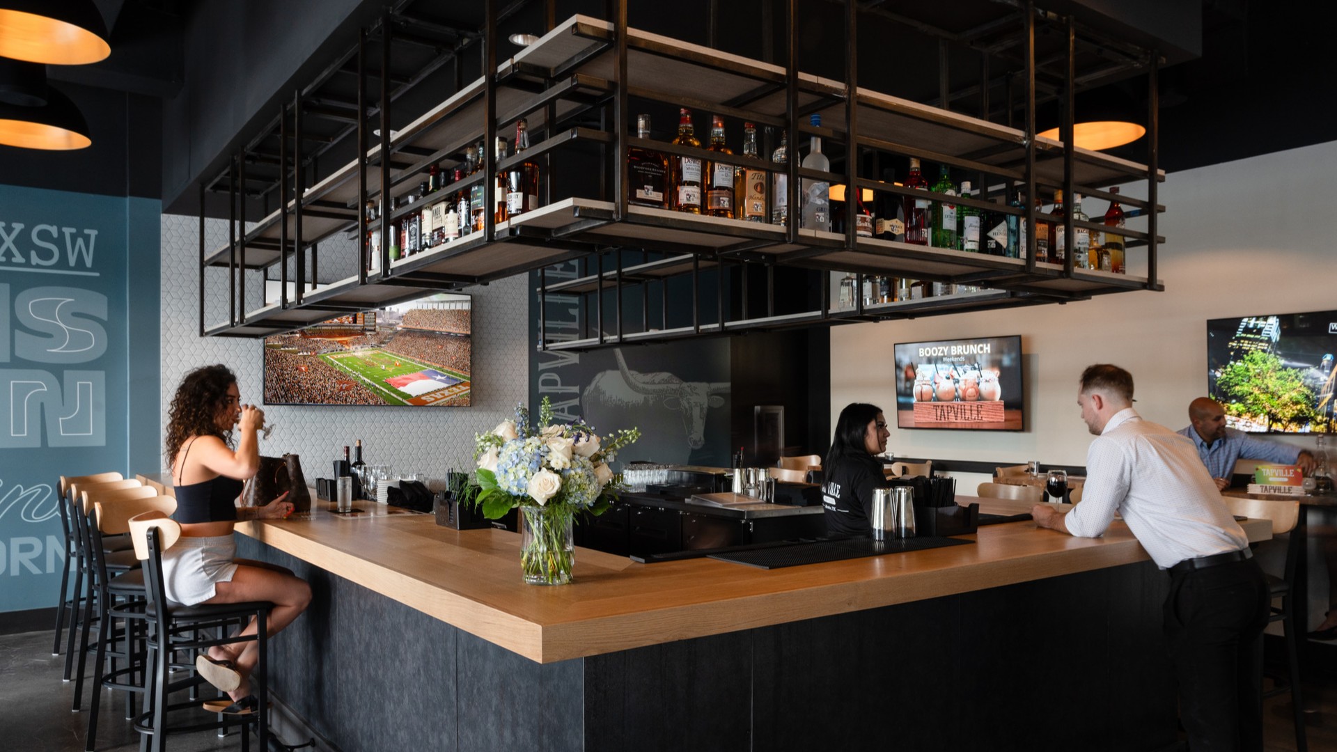 A man orders a beer from the right side of a minimalistic, modern bar as a woman drinks on the left side of the bar