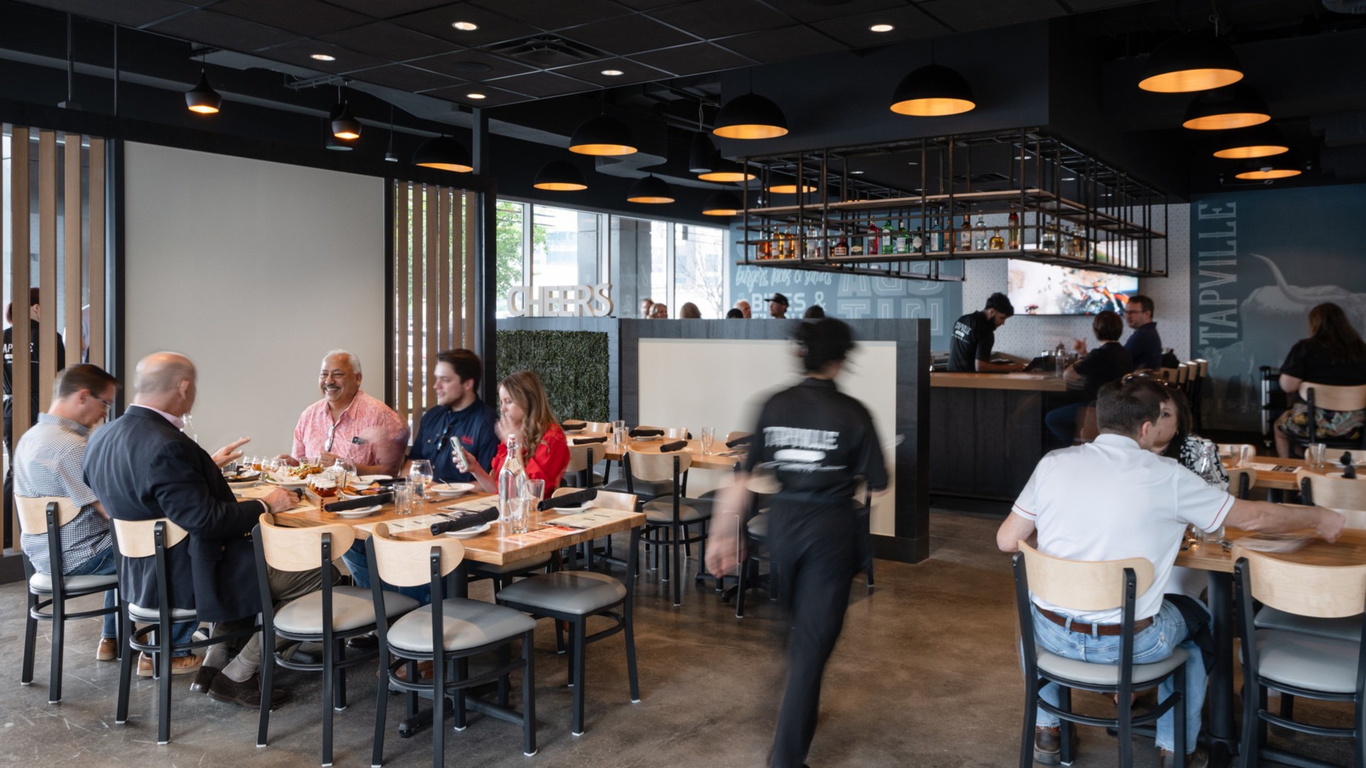A server walks towards the bar in a busy modern restaurant