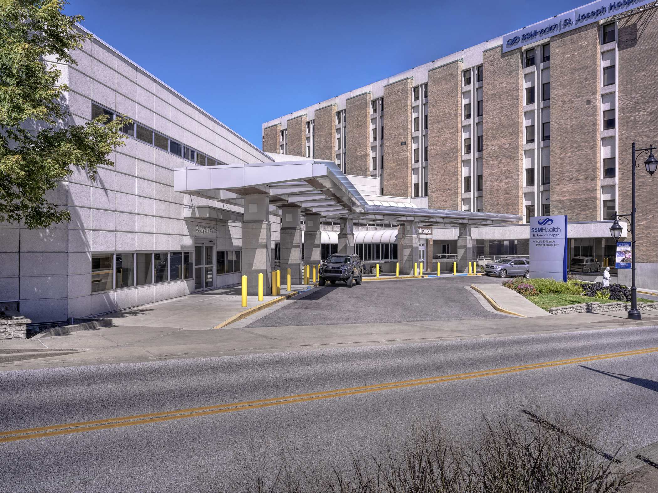 A wide image taken in daytime shows a modern entry canopy connecting two large, disparate hospital buildings