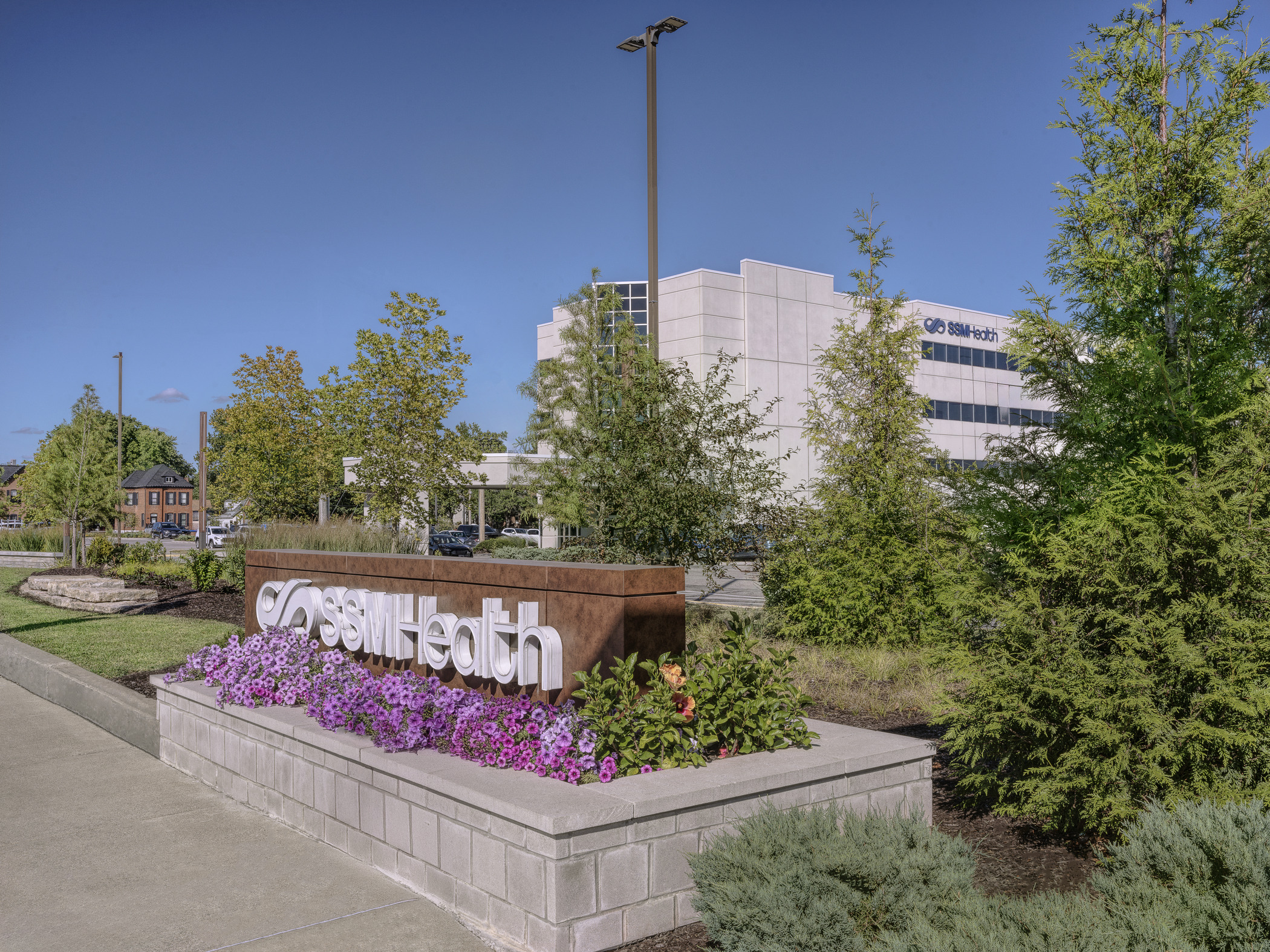 A hospital campus is photographed from the public sidewalk at daytime. The SSM Health logo is visible via a marquee sign in the foreground of the picture.
