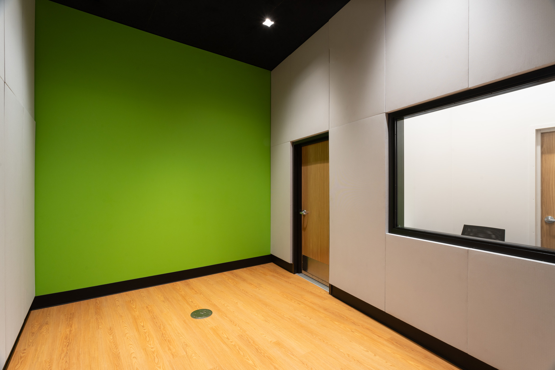 A modern studio office with lime green accent wall and wood flooring. A door and a window on the wall connects to the room next door.