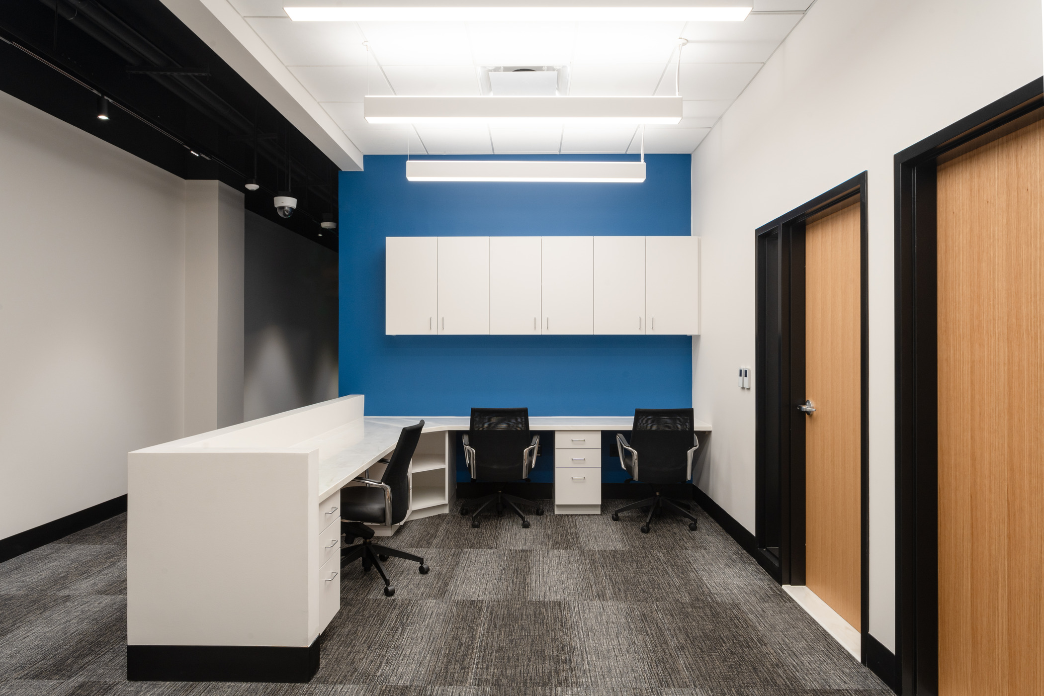 A lobby with blue accent wall with a white reception desk with 3 empty seats.