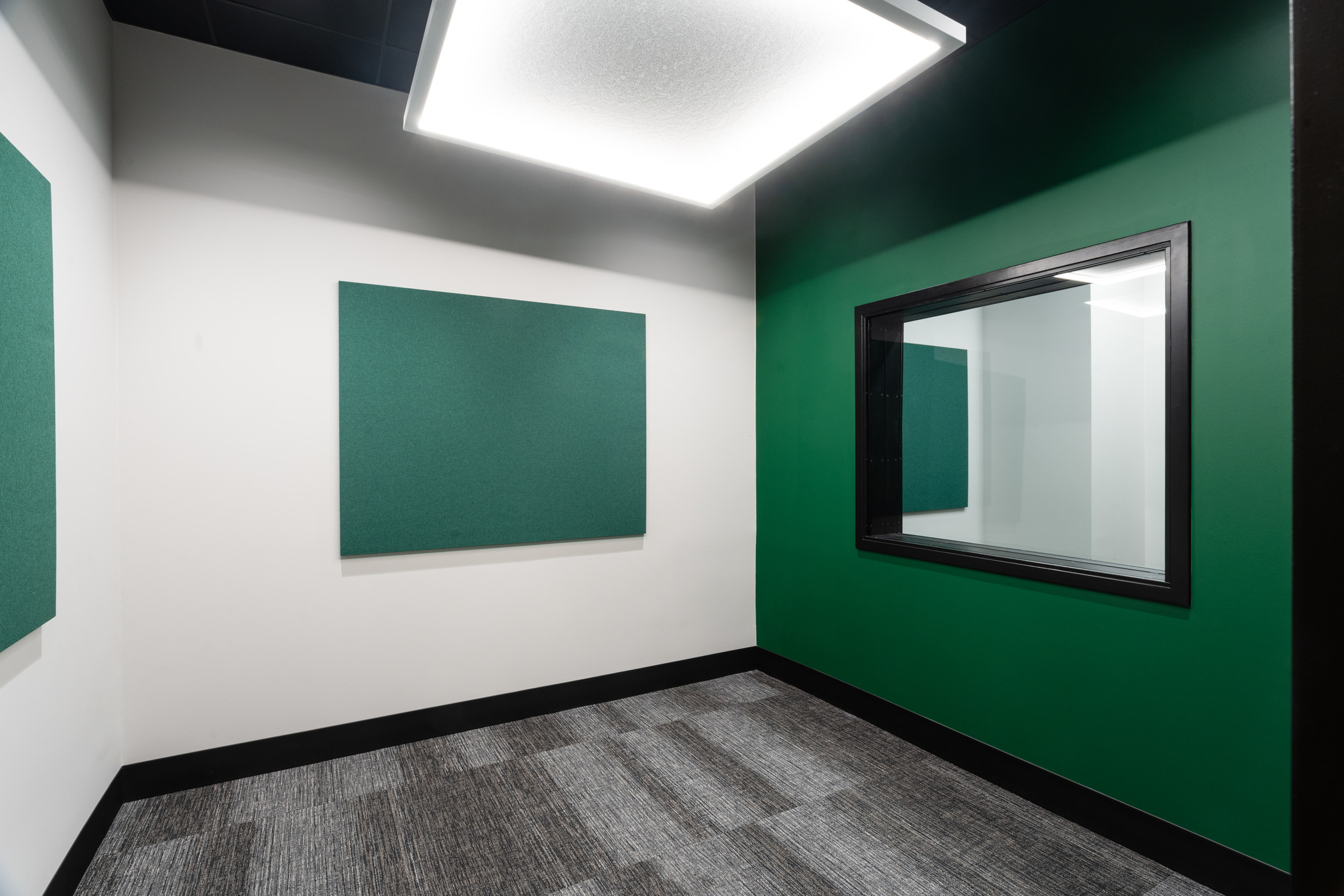 A modern empty office room with green board on the wall. A green accent wall with window to see through to another room next door.