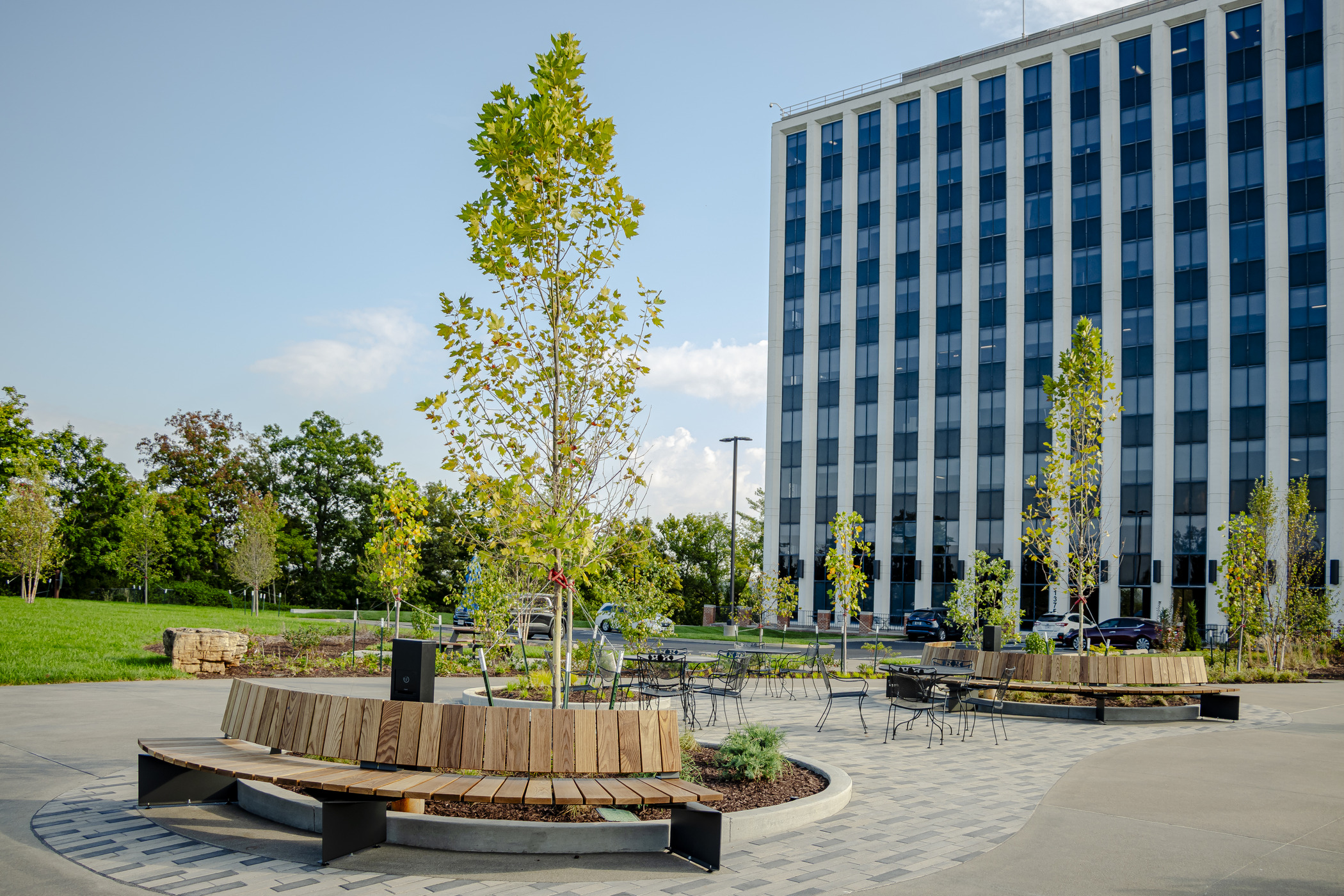 Contemporary office plaza with curved seating, trees, and paved paths in front of a high-rise building, designed for employee engagement and outdoor events.