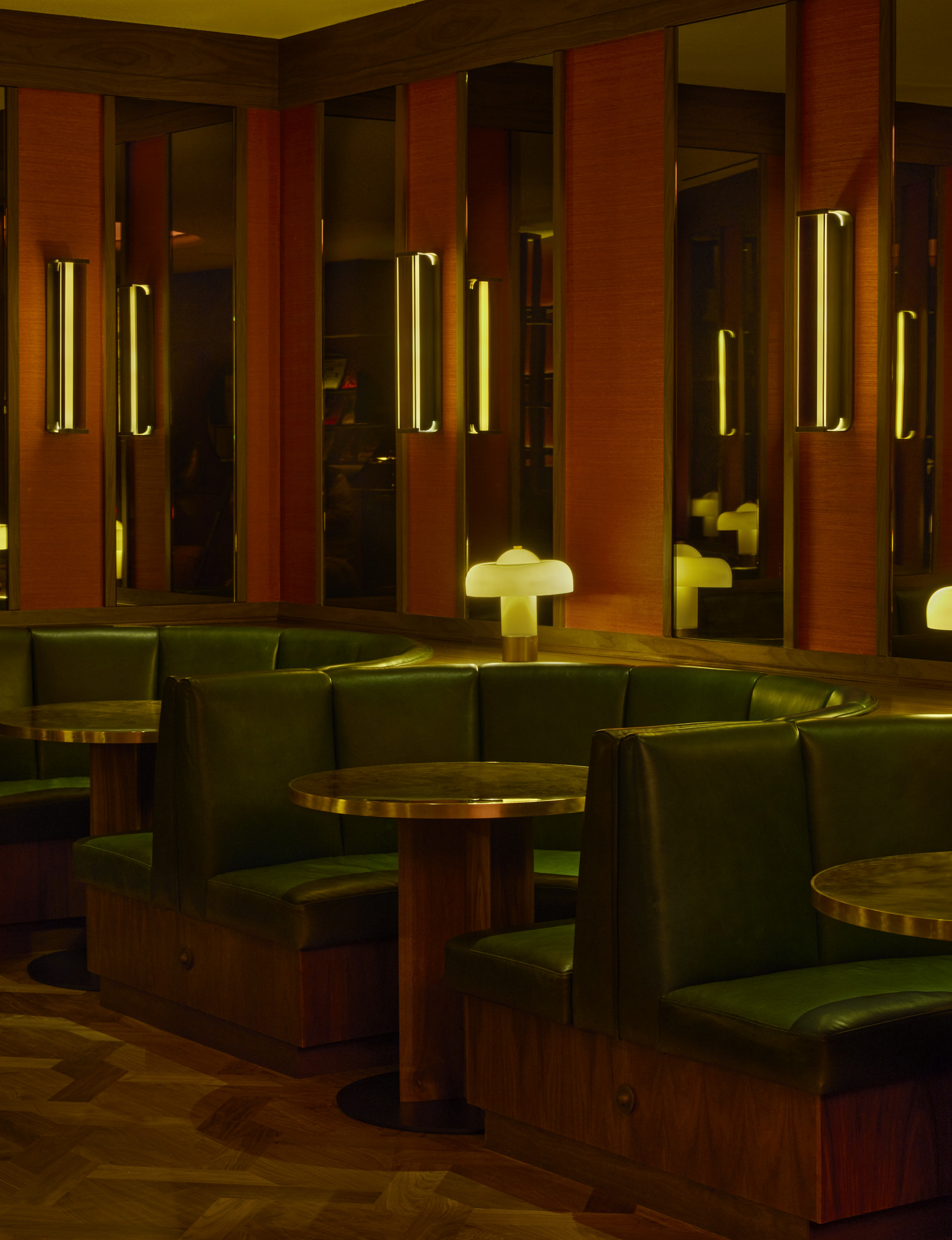 Restaurant interior design featuring green leather booths, round wooden tables, and warm ambient lighting. Rich wood paneling and mirrored accents showcase high-end hospitality architecture and bespoke restaurant design.