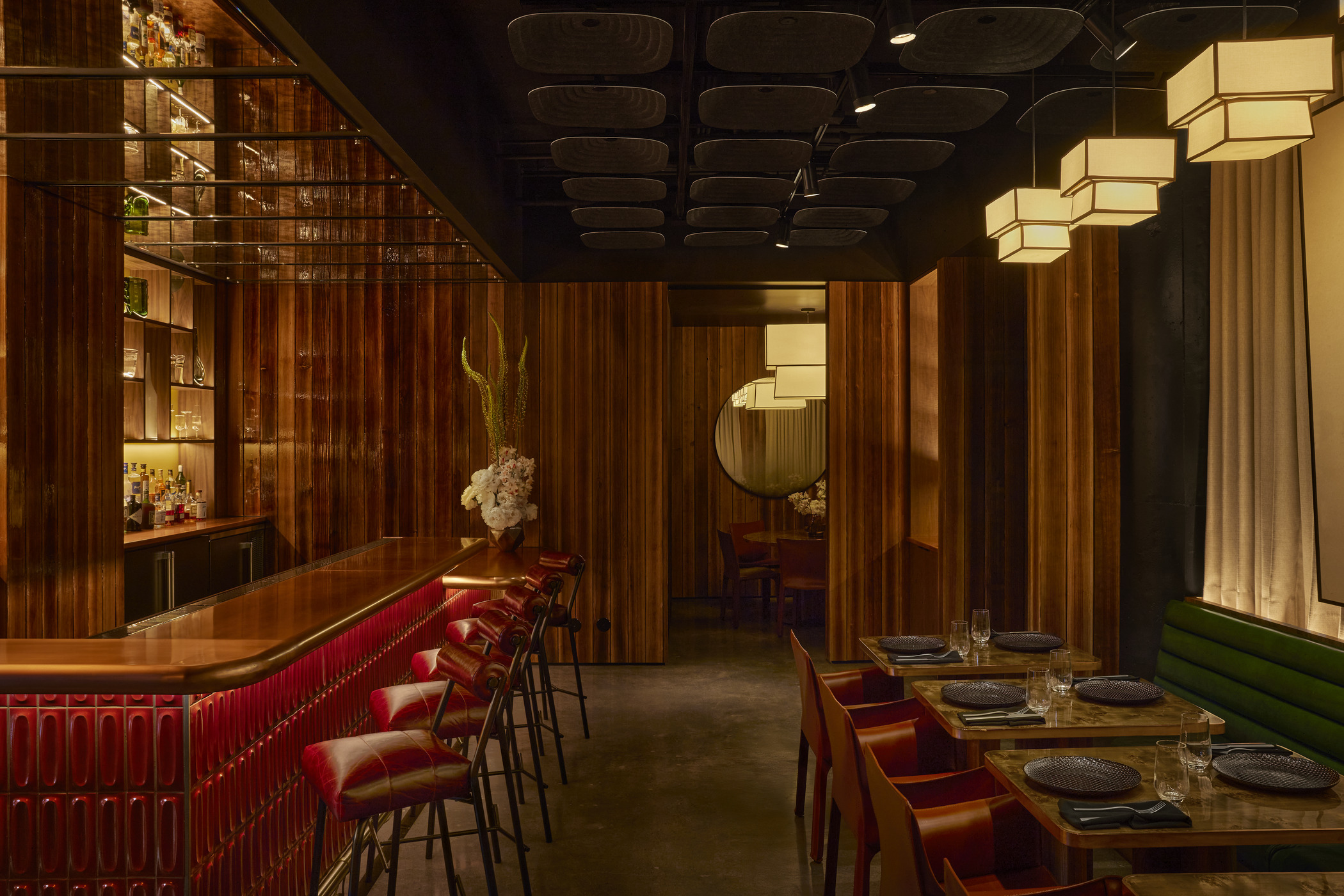 Restaurant interior in San Francisco showcasing a stylish bar with red accents and adjacent dining tables. Warm wood finishes and layered lighting emphasize modern hospitality architecture and intimate lounge design